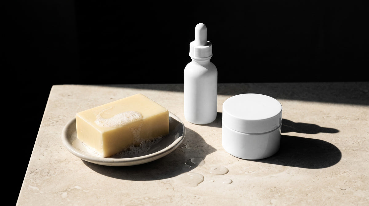 Kojic acid soap bar beside a serum bottle and cream jar — rinse-off vs leave-on kojic acid for dark spots