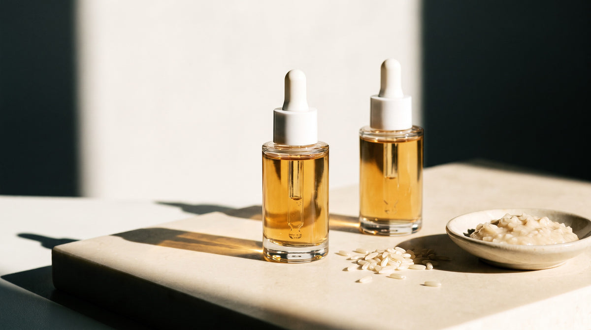 Kojic acid serum in a glass dropper bottle beside rice grains, referencing kojic acid's origin in rice fermentation