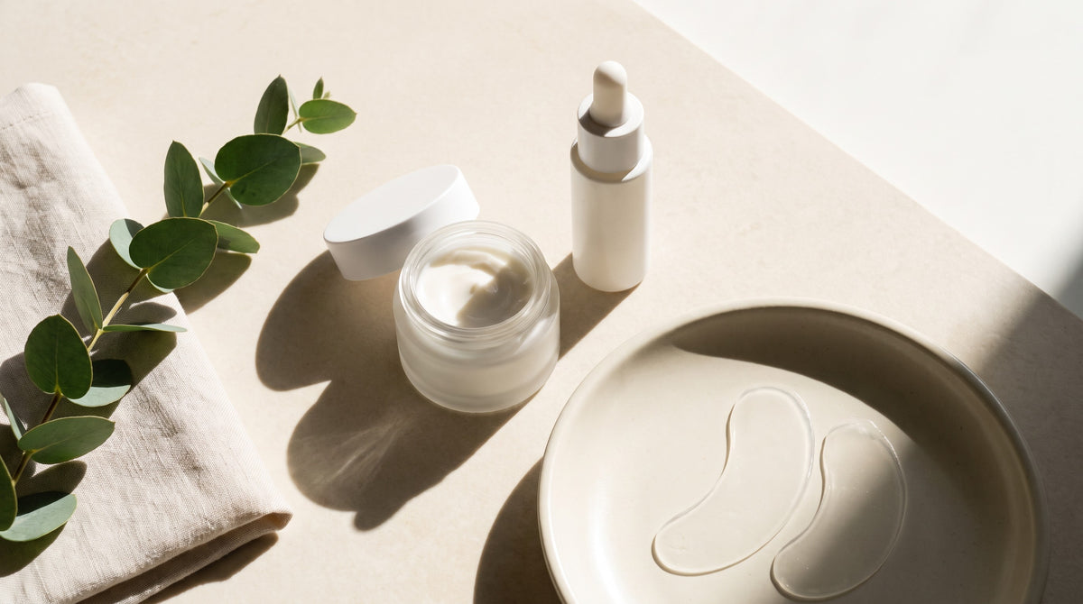 How to apply eye cream — eye cream jar, eye serum dropper and hydrogel under-eye patches on a cream stone surface