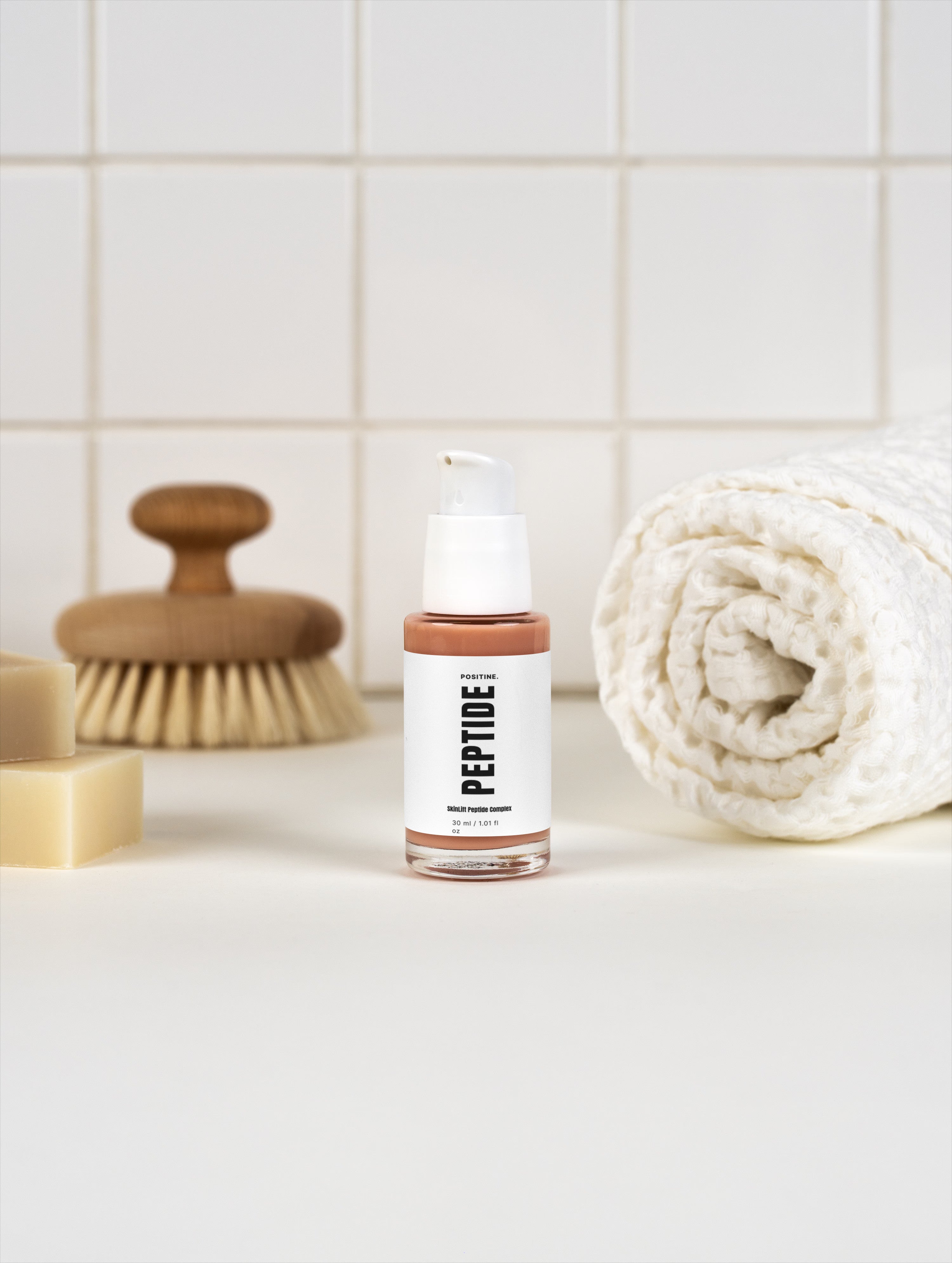 Complejo de péptidos SkinLift — frasco junto a una toalla enrollada y un cepillo de madera