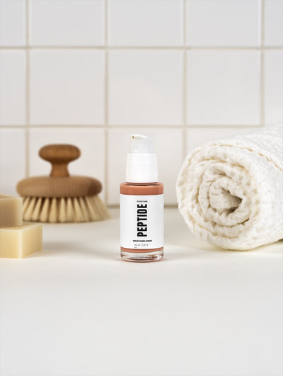 Complejo de péptidos SkinLift — frasco junto a una toalla enrollada y un cepillo de madera