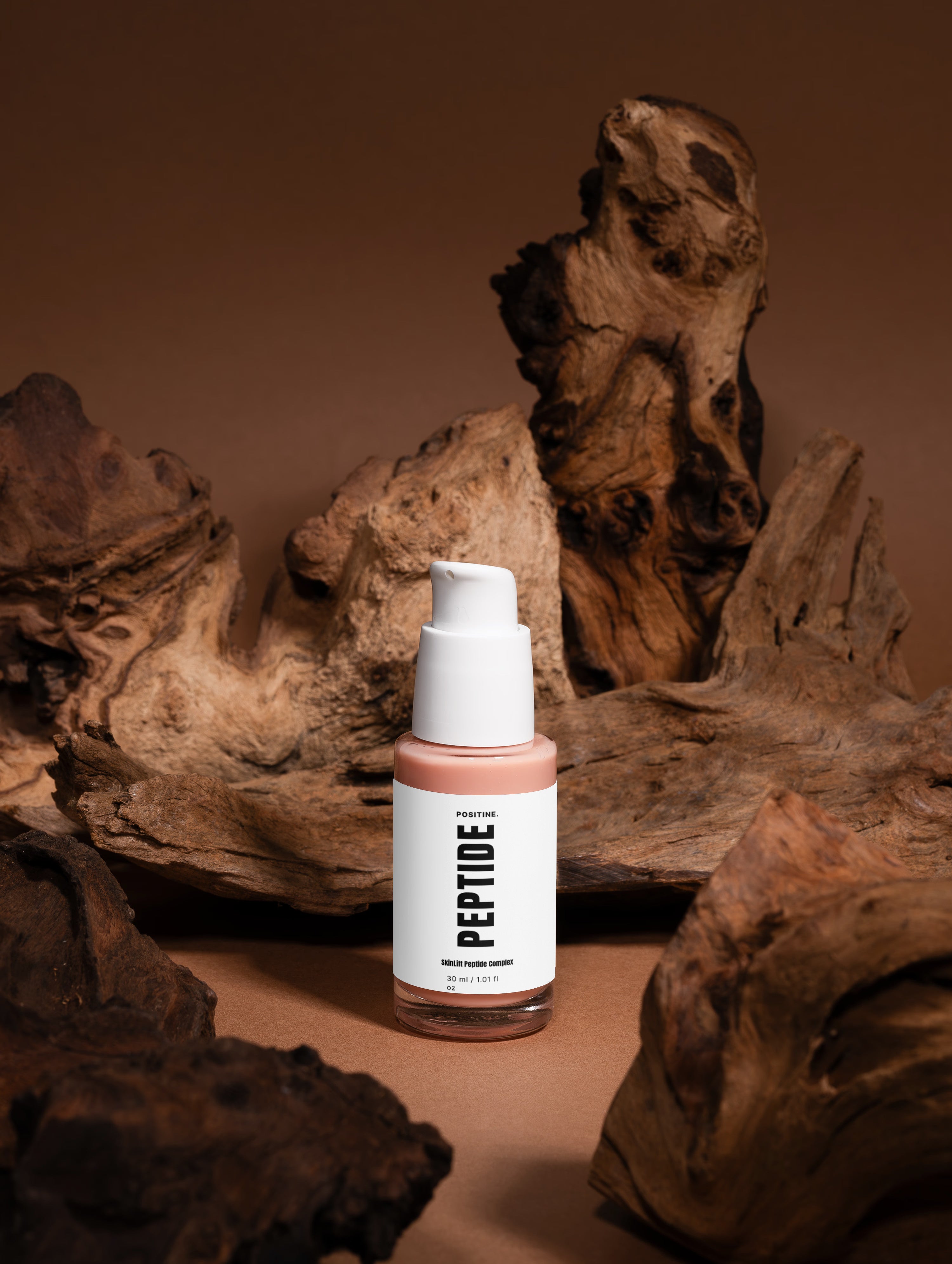 Complejo de péptidos SkinLift — frasco entre piezas de madera escultóricas sobre fondo marrón